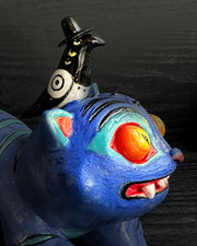 Colorful cat-like creature with large eyes and a small bird figure on its back against a dark background
