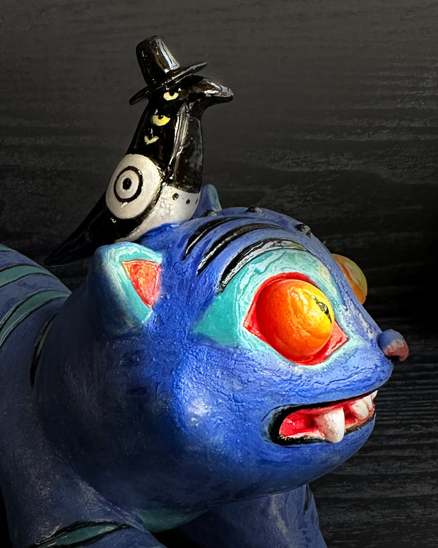 Colorful cat-like creature with large eyes and a small bird figure on its back against a dark background