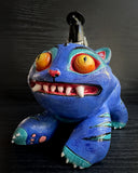 Colorful cat-like creature with large eyes and a small bird figure on its back against a dark background