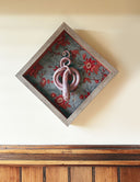 Ceramic sculpture of a reddish purple snake, seen from above. Its body is coiled into a spiral with its tail looping around itself. It sits inside of a wood shadowbox with red floral fabric lining the back and red fabric lining the inner borders.