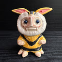 Ceramic figurine sculpture of a beige, yellow and black moth monster with round black eyes and small fangs.