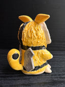 Ceramic figurine sculpture of a beige, yellow and black moth monster with round black eyes and small fangs.