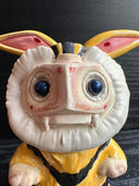Ceramic figurine sculpture of a beige, yellow and black moth monster with round black eyes and small fangs.