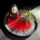 Ceramic plate with a small No Face figurine and air plant on a dark surface