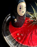 Ceramic plate with a small No Face figurine and air plant on a dark surface