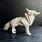 Off white ceramic sculpture of a wolf seemingly made out of paper, folded like an origami sculpture. 
