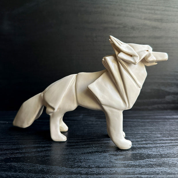 Off white ceramic sculpture of a wolf seemingly made out of paper, folded like an origami sculpture. 