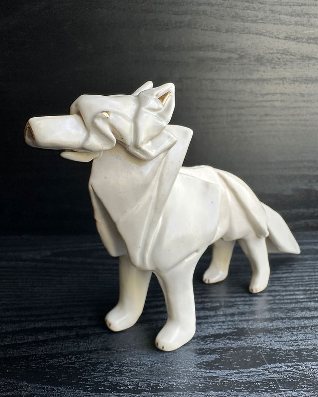Off white ceramic sculpture of a wolf seemingly made out of paper, folded like an origami sculpture. 