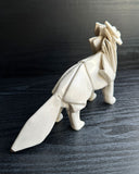 Off white ceramic sculpture of a wolf seemingly made out of paper, folded like an origami sculpture. 