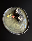 Two black soot sprites with white eyes on a dark plate with a greenish tint and small colorful stars.