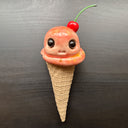 Ceramic figure of an ice cream cone with large cartoon style eyes and a cherry on top. 