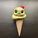 Ceramic figure of an ice cream cone with large cartoon style eyes and a cherry on top. 