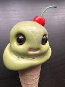Ceramic figure of an ice cream cone with large cartoon style eyes and a cherry on top. 
