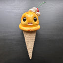 Ceramic figure of an ice cream cone with large cartoon style eyes and a cherry on top. 