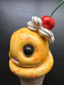 Ceramic figure of an ice cream cone with large cartoon style eyes and whipped cream and a cherry on top. 
