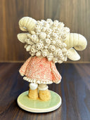Ceramic figurine of a cute anthropomorphic sheep, with large shiny eyes and curled horns. She wears a pink textured sweater and tennis shoes.