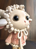 Ceramic figurine of a cute anthropomorphic sheep, with large shiny eyes and curled horns. She wears a pink textured sweater and tennis shoes.