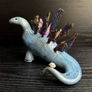 Ceramic sculpture of a blue dinosaur with sharp, colorful crystals sticking out of its back.