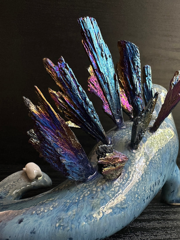 Ceramic sculpture of a blue dinosaur with sharp, colorful crystals sticking out of its back.