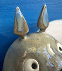 Ceramic sculpture of Totoro, positioned on a tree branch and playing a small wind instrument. Next to him are tiny Chibi Totoro, also playing instruments. Background is a circular blue sky with a giant moon.