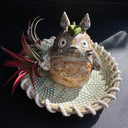 Ceramic sculpture of Totoro in a ceramic plate with cord tied around it.