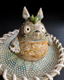  Ceramic sculpture of Totoro in a ceramic plate with cord tied around it.