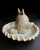 Ceramic sculpture of Totoro in a ceramic plate with cord tied around it.