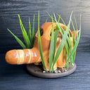 Ceramic sculpture of the Catbus from My Neighbor Totoro, with smaller proportions than usual to depict it as a kitten. Inside it is a small girl with a surprised expression. A small white chibi Totoro stands in front of the cat on a base with fake grass and small stones.