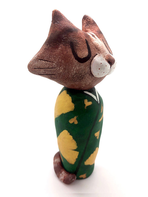 Sculpture of a large headed cartoon cat, wearing a green kimono with gold gingko leaves over it. Its eyes are closed and it has a content expression on its face.