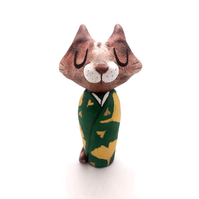 Sculpture of a large headed cartoon cat, wearing a green kimono with gold gingko leaves over it. Its eyes are closed and it has a content expression on its face.