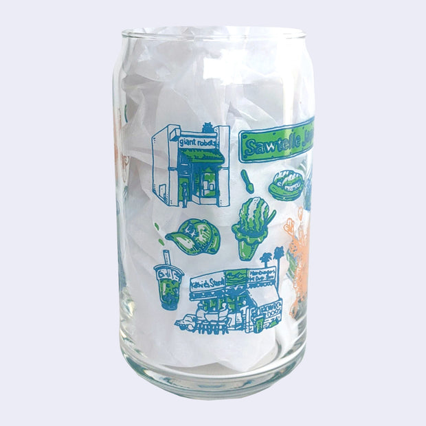 Glass cup with a flat base and slightly inward lip, it has printed design all over the cup. Various illustrations are within a color scheme of blue, green, orange. Illustrations include GR2, shaved ice, a LA cap, and Ketchie's food stand.