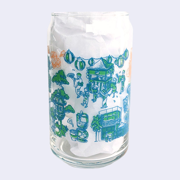 Glass cup with a flat base and slightly inward lip, it has printed design all over the cup. Various illustrations are within a color scheme of blue, green, orange. Illustrations include kimono clad people dancing, lanterns, Tsujita, and drip coffee.