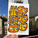 Paper with illustrations on it of several stylized Garfield heads, held in someone's hand in front of buildings.