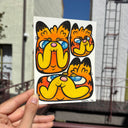 Paper with illustrations of 3 cartoon cat heads, stylized versions of Garfield held in someone's hand.