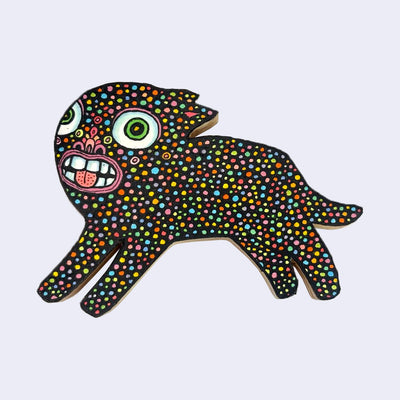 Illustration made with many lines, giving it the feel of a folk art woodcut on a die cut wood panel of an animal beast with a colorful polkadot body with very large eyes and a large toothy mouth.