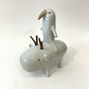 Ceramic sculpture of a bird like creature, white with smooth body and simplistic limbs riding atop of a capybara like creature with wooden branches for antlers.