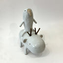 Ceramic sculpture of a bird like creature, white with smooth body and simplistic limbs riding atop of a capybara like creature with wooden branches for antlers.