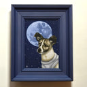 A framed dog portrait featuring a small brown and white dog wearing a white astronaut suit against a dark blue starry night sky with a large full moon. The artwork is housed in a thick, dark navy blue frame and is mounted on a light beige wall.
