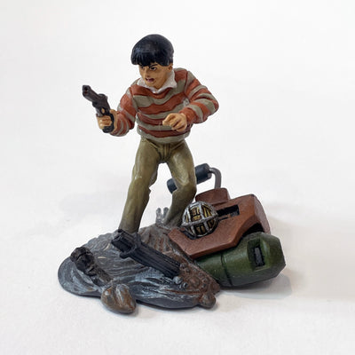 Vinyl figure of a boy wearing a striped shirt, standing atop a melted pile of gray goo. He holds a gun and has an angry expression.