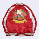 Back view of Sukajan style bomber jacket with a red semi shiny body with ivory colored sleeves and color accents. Bottom of the sleeves and jacket have a white and red striped band. A large graphic of Hello Kitty with red roses is on the back.