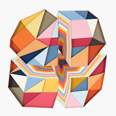 Geometric designed layered cut paper sculpture, creating a three dimensionality. A vertical and horizontal cross section of a 10 sided shape reveals many layers. Colors are earthy toned browns, oranges, yellows, blues and reds.