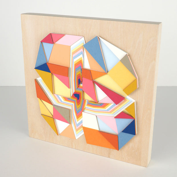 Geometric designed layered cut paper sculpture, creating a three dimensionality. A vertical and horizontal cross section of a 10 sided shape reveals many layers. Colors are earthy toned browns, oranges, yellows, blues and reds. Shown at the side.