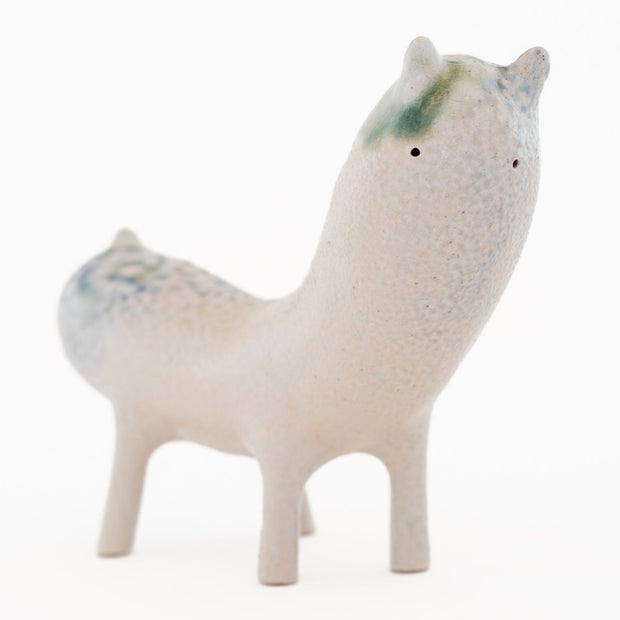 Ceramic sculpture of a long bodied, skinny character with small ears and eyes standing on 4 short legs.