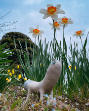 Ceramic sculpture of a long bodied, skinny character with small ears and eyes standing on 4 short legs.