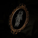 An ornate oval framed artwork featuring a white line drawing of a ghostly figure on a black background, set against a dark draped backdrop.
