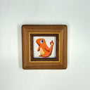 A small framed art piece featuring a stylized painting of Charmander, set inside a square wooden frame with a gold inner trim, displayed against a plain white background.