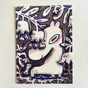 A whimsical cartoon illustration of a white creature with a large oval eye, surrounded by stylized white flowers and leaves on a brown background, photographed against a light off-white wall.
