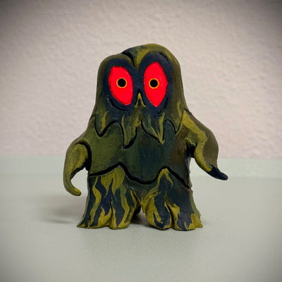 Sculpture of Hedorah, a pollution smoke monster, dark blue and yellowish green. It stands on 2 slimey legs and has large red eyes.