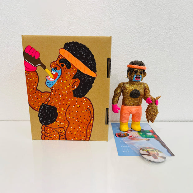 Gold glitter vinyl figure of a man, shirtless with short curly hair and chest hair. He holds a sparkly gold fish in his hands and stands besides a painted box.