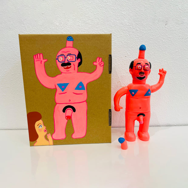 Neon pink painted soft vinyl figure of a nude man with glasses. He is balding with some facial hair and has a blue tipped penis atop his head. His nipples are blue and his own penis is also blue tipped. One of his hands is formed into a peace sign.